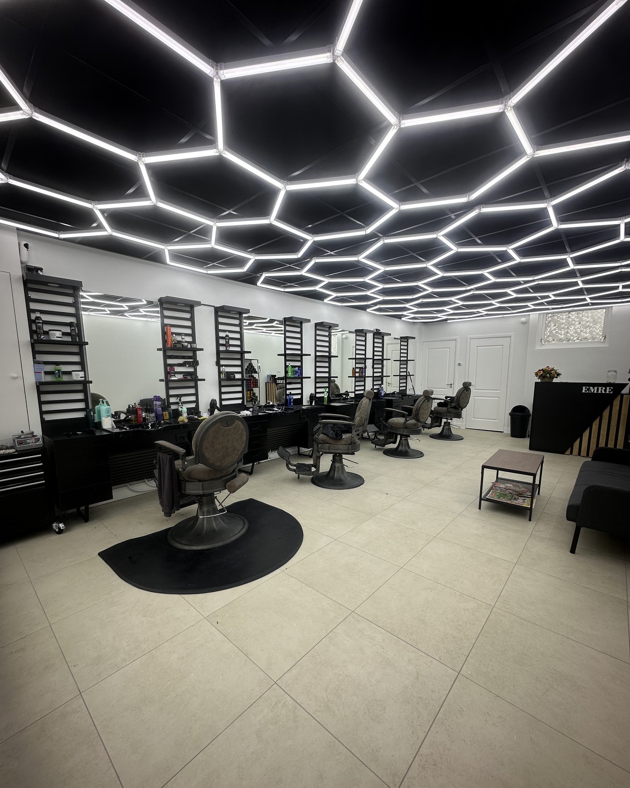 Een rij barberstoelen voor de spiegels, onder het verlichte zeshoekige plafond