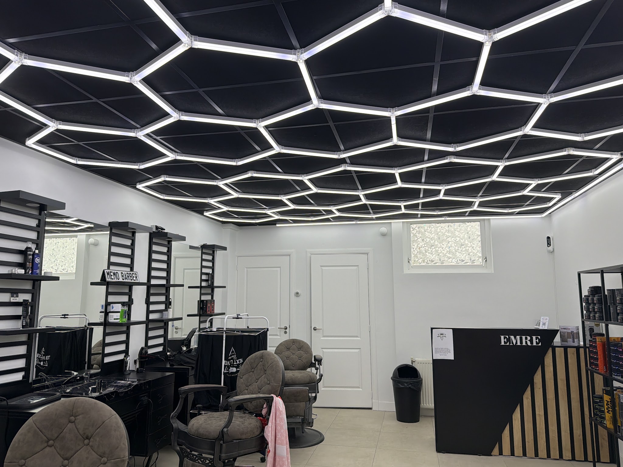 Het interieur van NextLevelBarber: barberstoelen onder het zeshoekige lichtplafond en de toonbank met EMRE erop